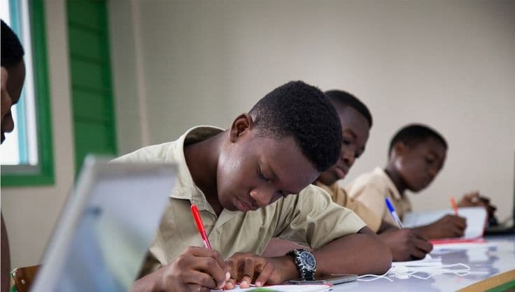 Trois jeunes étudiants africains concentrés écrivent avec application dans une salle de classe.