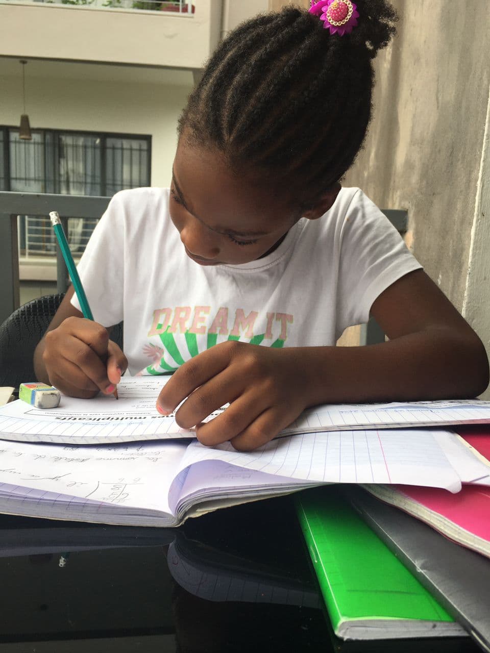 Jeune fille aux tresses écrivant avec concentration dans son cahier avec un crayon gris.