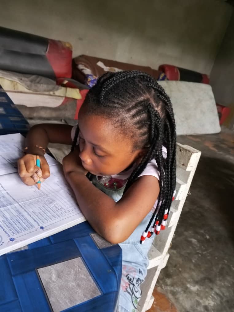 Jeune fille aux tresses perlées écrivant avec application dans son cahier d'exercices.